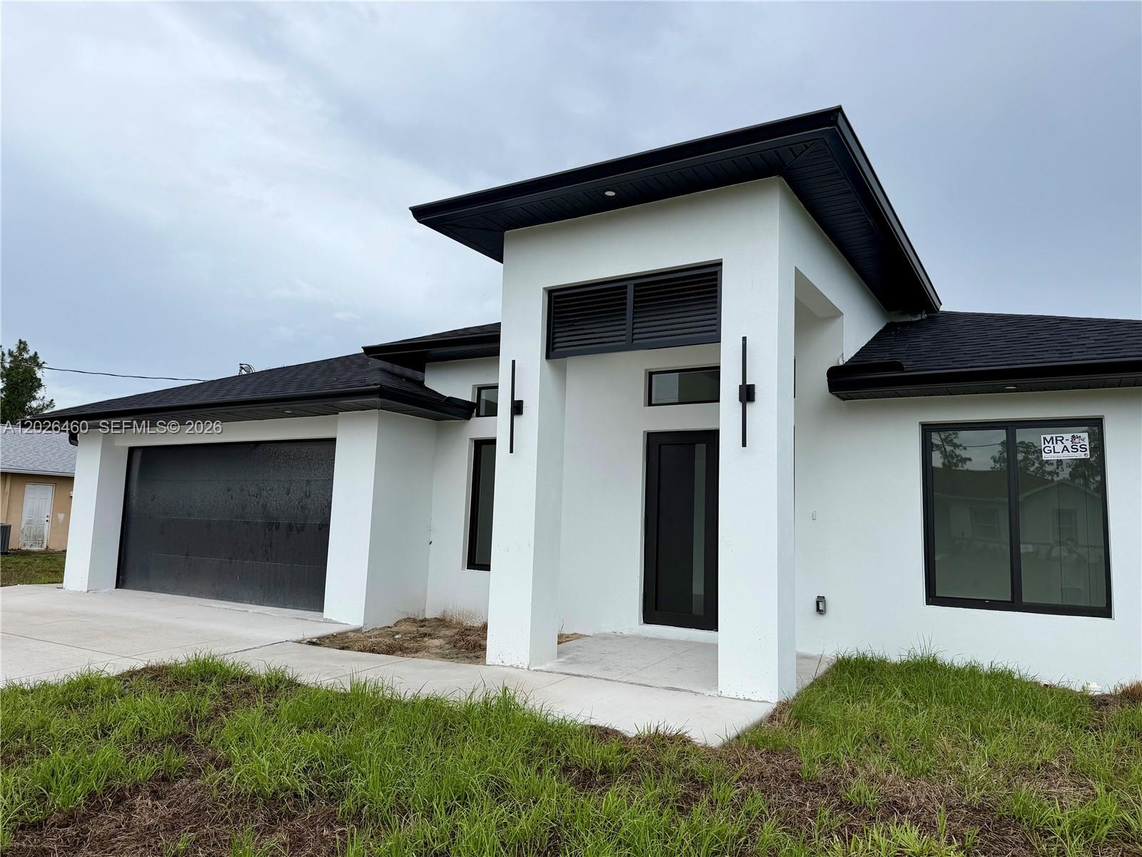 A modern, single-story house with white stucco walls, a black garage door, and a flat roof — 911 Cleveland Ave, Lehigh Acres FL 33972, LEHIGH ACRES, FL