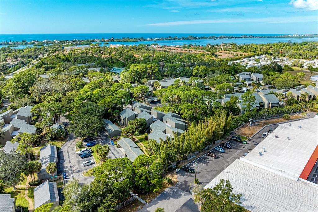 An aerial view shows a residential complex with gray-roofed buildings nestled among trees near water — 110 WOODLAND PLACE UNIT 110, OSPREY, FL
