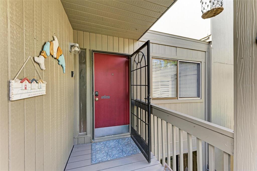 A red front door with a black security gate sits on a wooden porch — 110 WOODLAND PLACE UNIT 110, OSPREY, FL