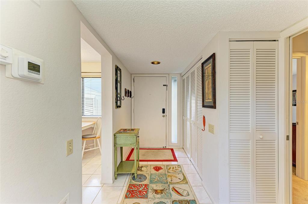 An entryway with white tile floors, a green side table, and louvered closet doors — 110 WOODLAND PLACE UNIT 110, OSPREY, FL