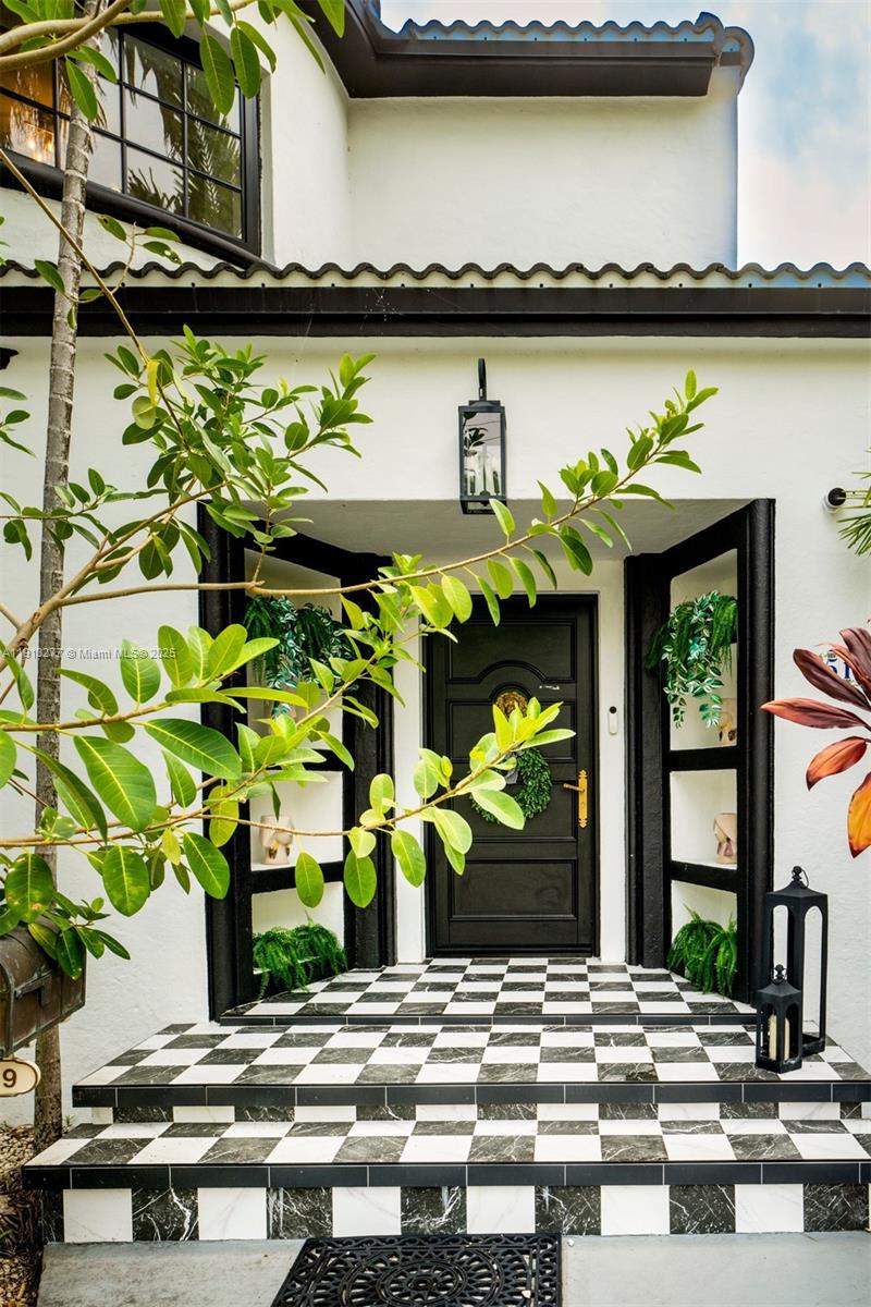 A black front door with a checkerboard tiled porch and built-in shelving with plants — 5149 Alton Rd, Miami Beach FL 33140, MIAMI BEACH, FL
