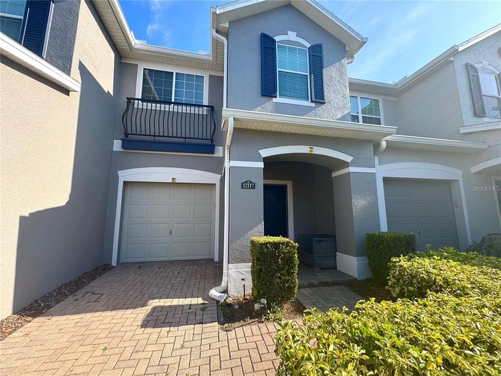 A two-story townhouse exterior features a single-car garage, a covered entryway, and blue shutters — 12117 CITRUSWOOD DRIVE, ORLANDO, FL