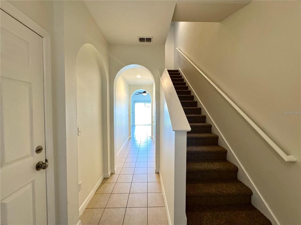 A hallway with tiled floors leads to a bright doorway beside a carpeted staircase — 12117 CITRUSWOOD DRIVE, ORLANDO, FL
