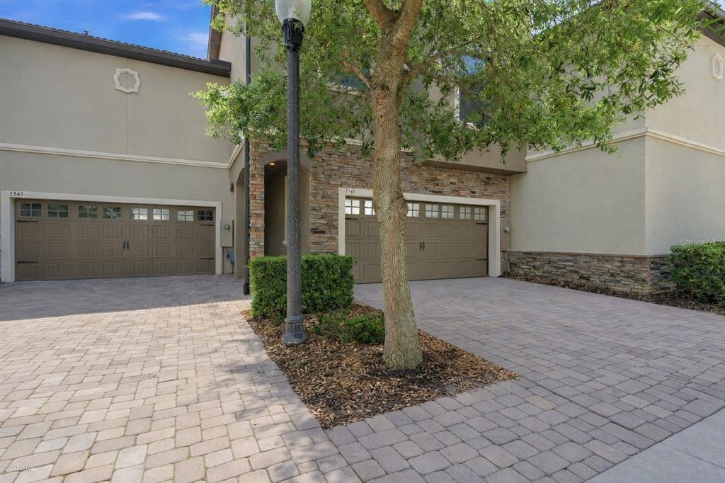 A two-story townhouse features a stone facade, two garage doors, and a paved driveway — 1341 SHINNECOCK HILLS DRIVE, DAVENPORT, FL