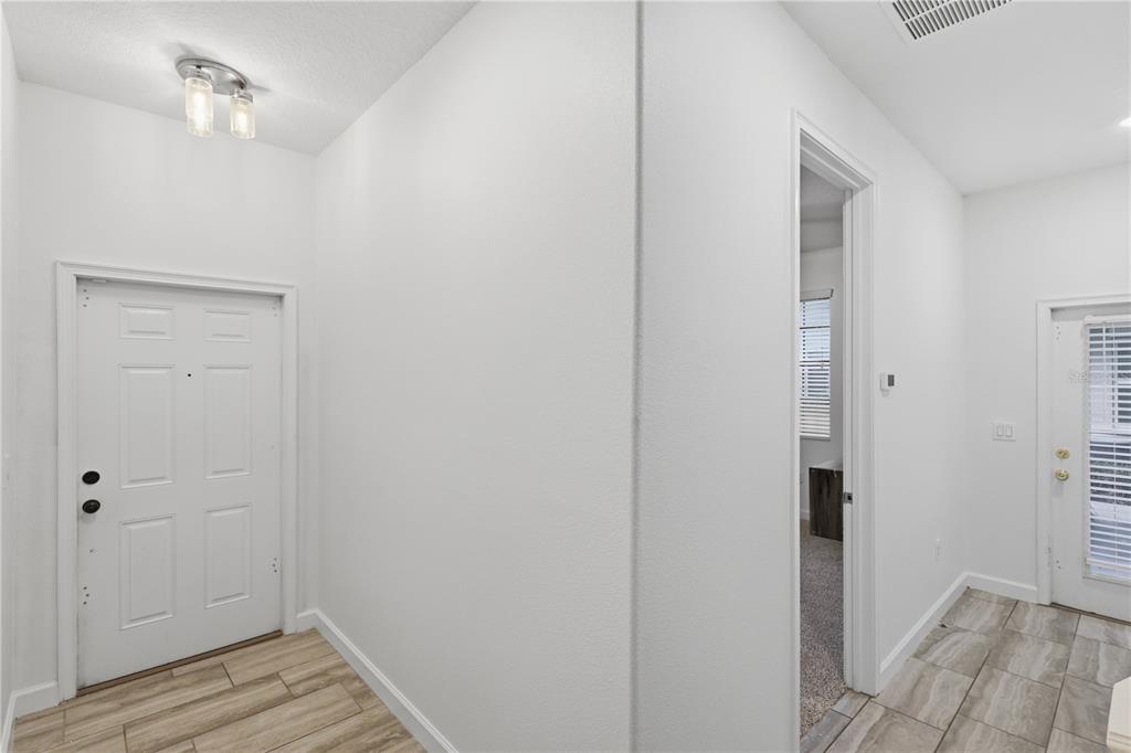 An entryway with light wood-look tile flooring, white walls, and a white front door — 1341 SHINNECOCK HILLS DRIVE, DAVENPORT, FL