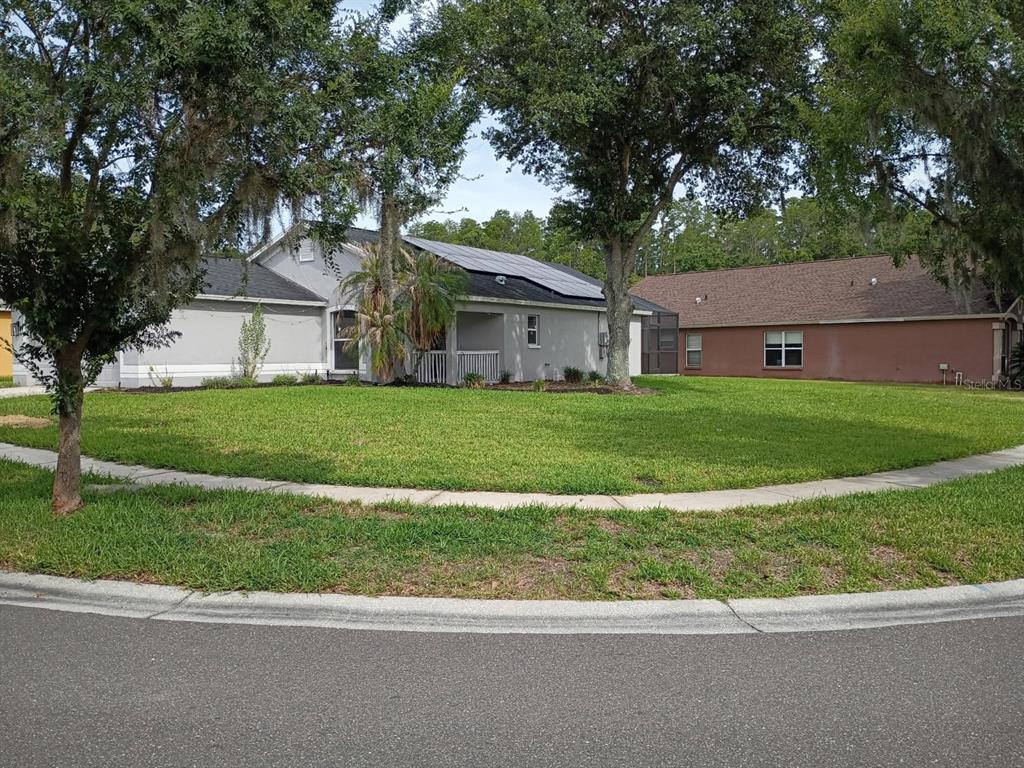 A gray house with solar panels on the roof sits on a corner lot — 30936 BURLEIGH DRIVE, WESLEY CHAPEL, FL