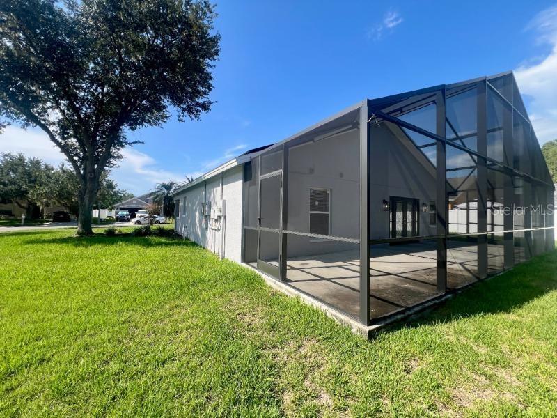 A side view of a house featuring a large screened-in patio and a grassy yard — 30936 BURLEIGH DRIVE, WESLEY CHAPEL, FL