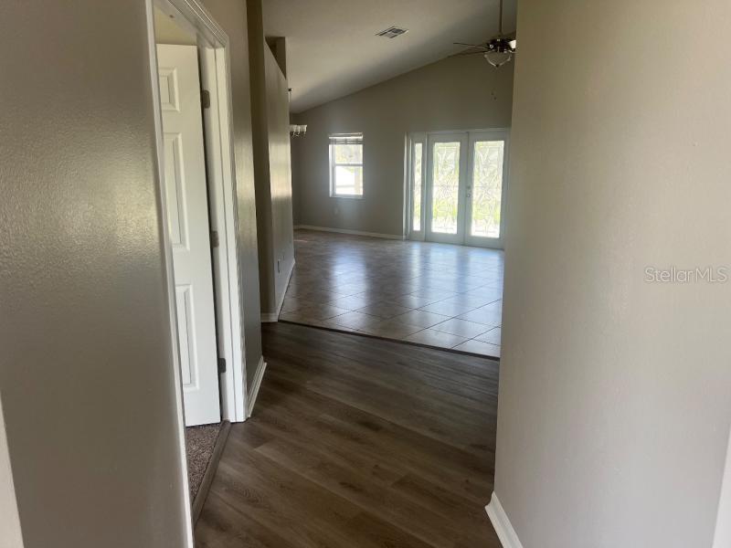 A hallway with wood-look flooring leads into a tiled living area with glass doors — 30936 BURLEIGH DRIVE, WESLEY CHAPEL, FL