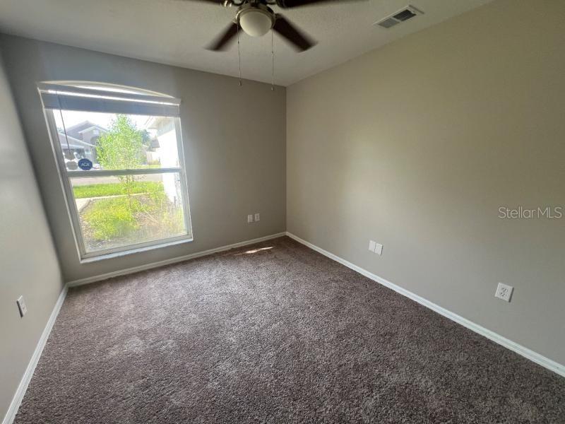 An empty bedroom features gray walls, brown carpet, a ceiling fan, and a large window — 30936 BURLEIGH DRIVE, WESLEY CHAPEL, FL
