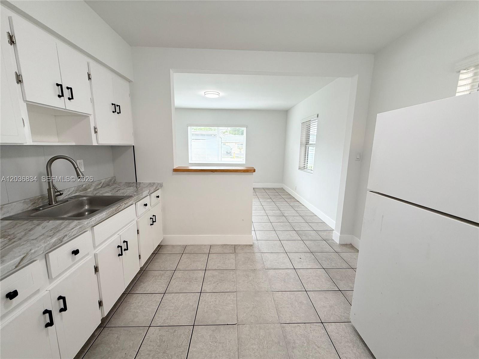 A kitchen with white cabinets, a marble-look countertop, and tile flooring opens to a room — 2215 Madison St # 5, Hollywood FL 33020, HOLLYWOOD, FL