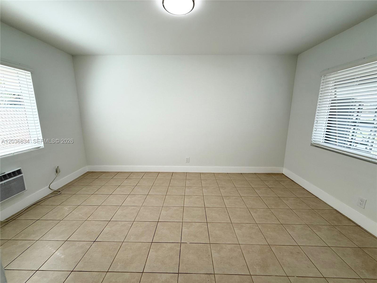 An empty room features light-colored walls, beige tile flooring, and two windows with blinds — 2215 Madison St # 5, Hollywood FL 33020, HOLLYWOOD, FL