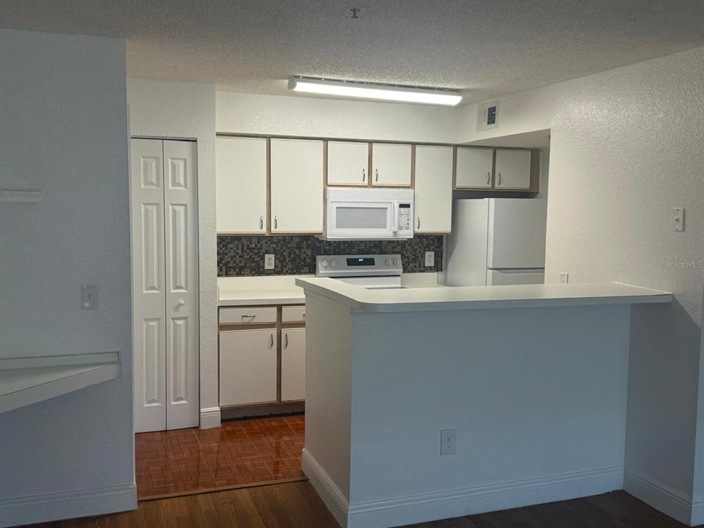 A kitchen features white cabinets, a mosaic tile backsplash, and a breakfast bar — 2202 KEY WEST COURT UNIT 626, KISSIMMEE, FL