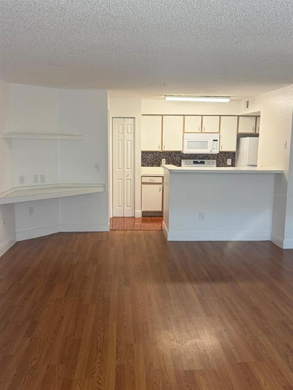 A kitchen with white cabinets and a breakfast bar overlooks a room with wood flooring — 2202 KEY WEST COURT UNIT 626, KISSIMMEE, FL