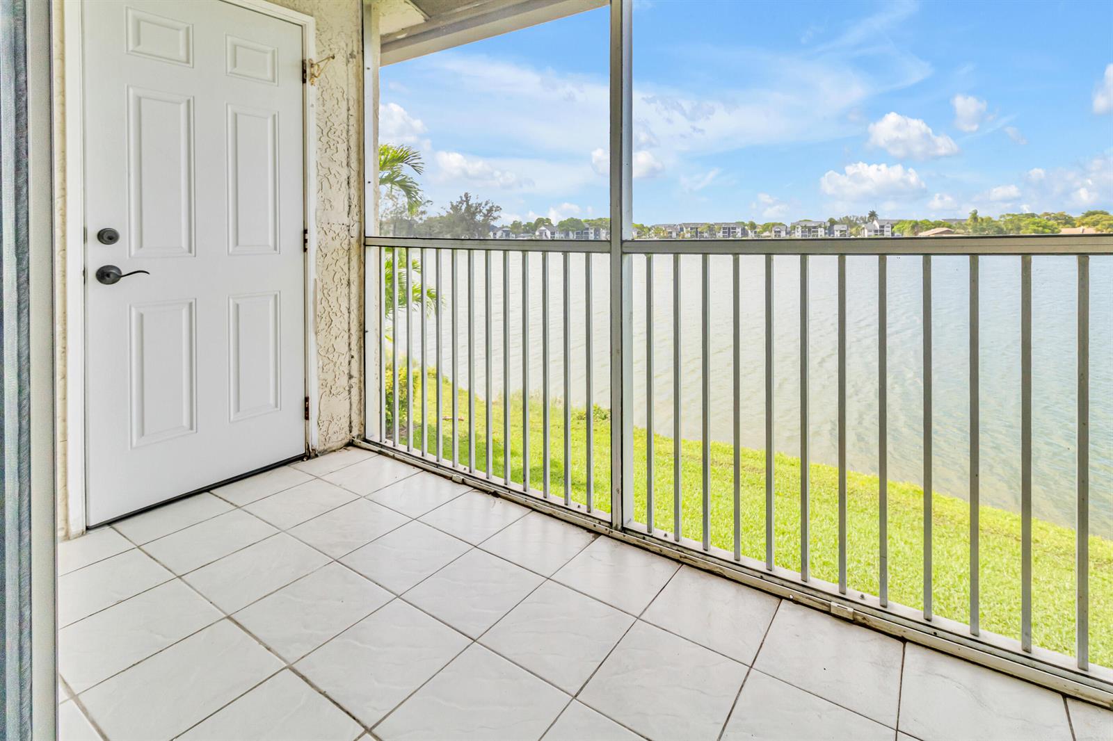 A tiled balcony with a white door overlooks a lake and a grassy lawn — 5510 Lakeside Drive # 202, Margate FL 33063, MARGATE, FL