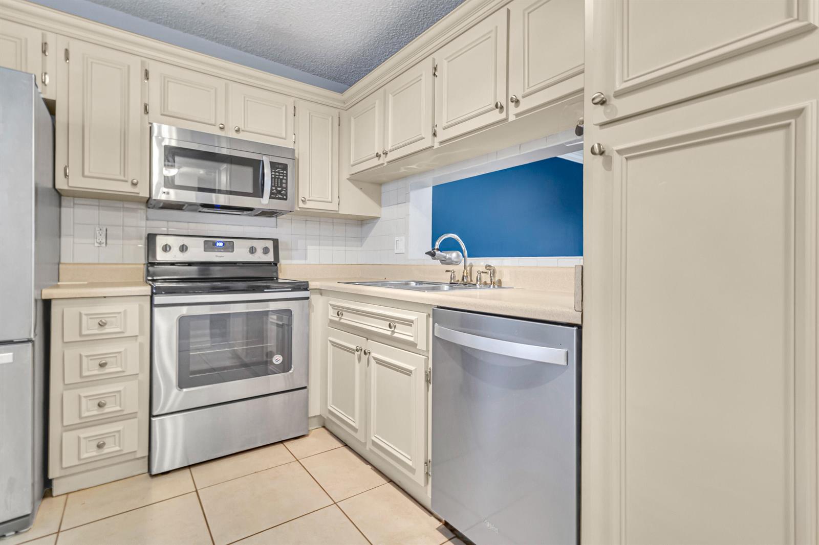 A kitchen features cream-colored cabinets, stainless steel appliances, a tiled backsplash, and light-colored countertops — 5510 Lakeside Drive # 202, Margate FL 33063, MARGATE, FL