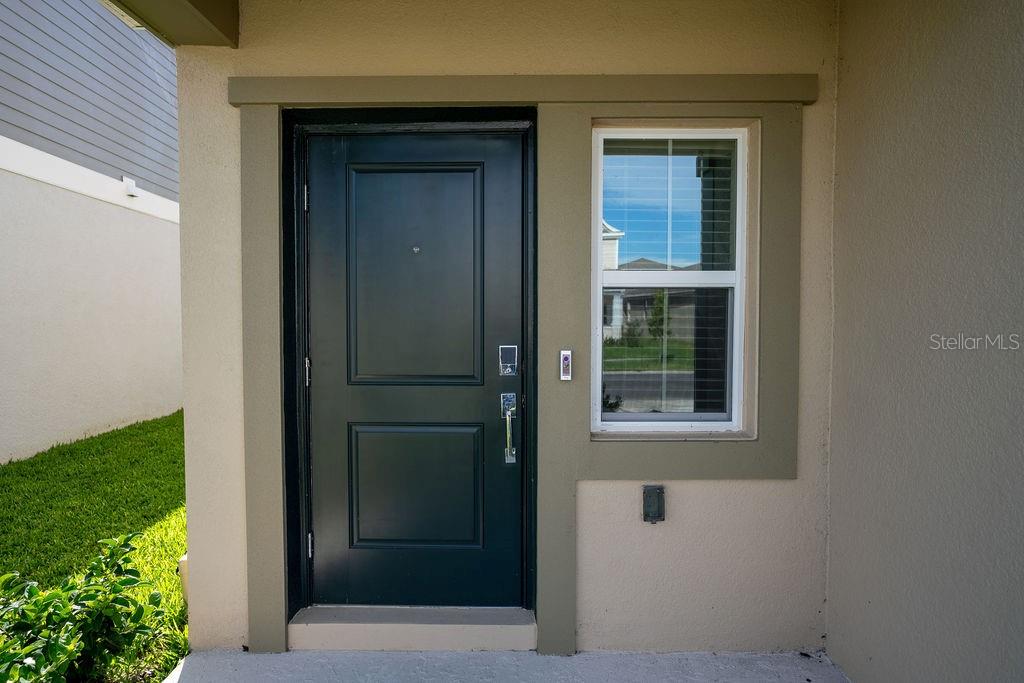 A dark front door with a window and a doorbell sits on a concrete porch — 223 BRAVE ROAD, DAVENPORT, FL