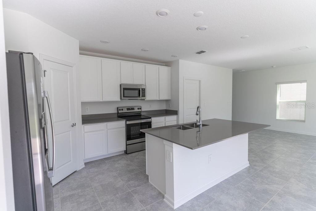 A kitchen features white cabinets, gray countertops, a center island, and stainless steel appliances — 223 BRAVE ROAD, DAVENPORT, FL
