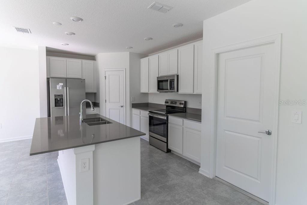 A modern kitchen features white cabinets, gray countertops, stainless steel appliances, and a central island — 223 BRAVE ROAD, DAVENPORT, FL