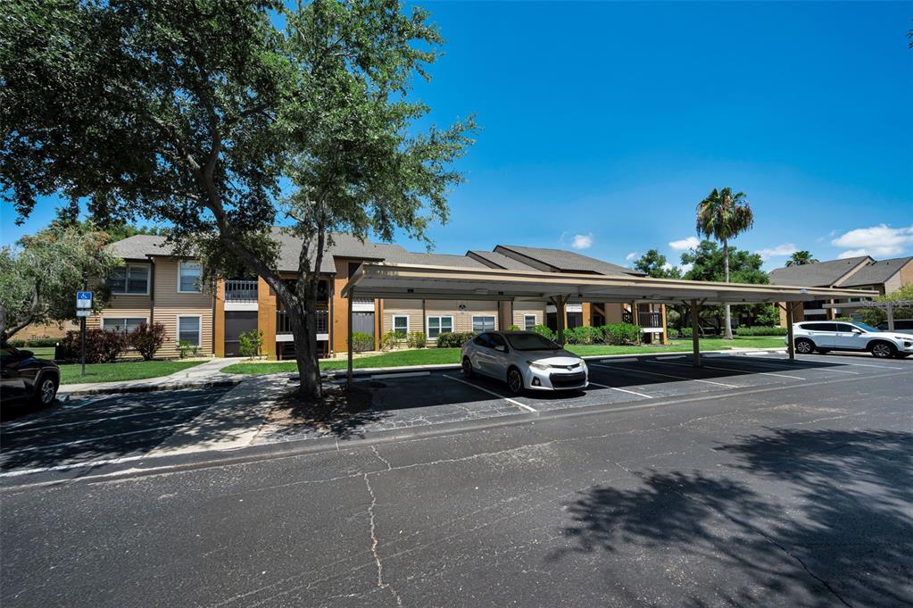 A parking lot with a covered carport sits in front of a multi-story apartment building — 500 BELCHER ROAD S UNIT 108, LARGO, FL