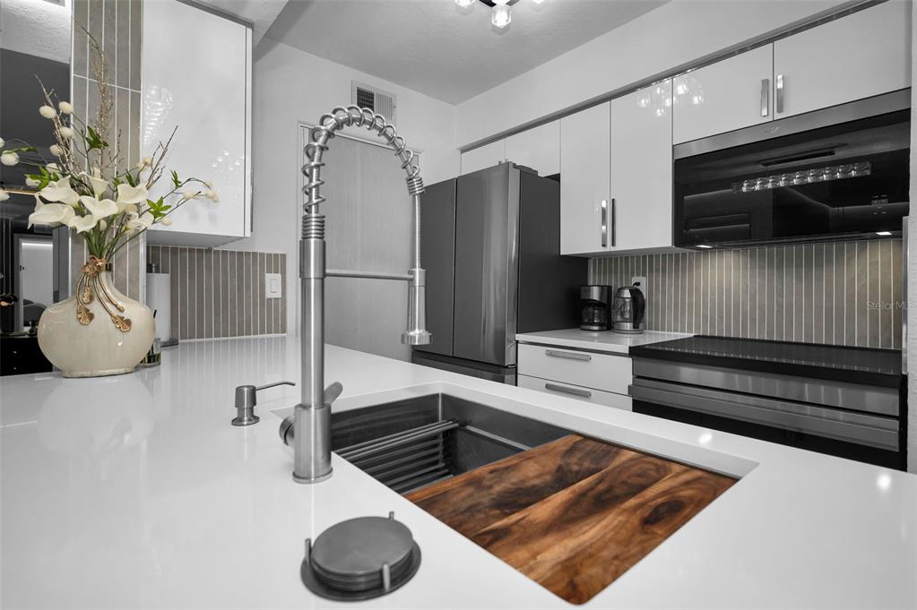 A modern kitchen features white cabinets, a stainless steel refrigerator, and a large farmhouse sink — 500 BELCHER ROAD S UNIT 108, LARGO, FL