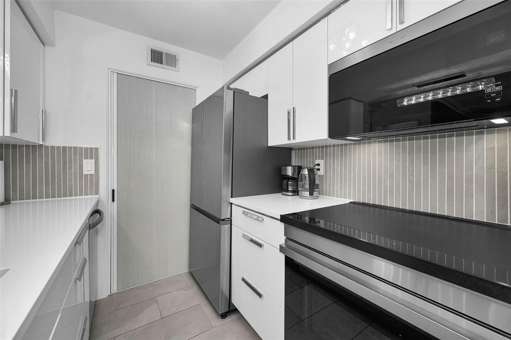 A modern kitchen features white cabinets, stainless steel appliances, and a gray tiled backsplash — 500 BELCHER ROAD S UNIT 108, LARGO, FL