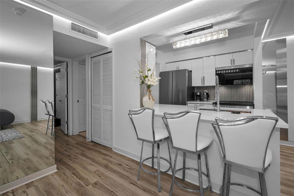 A modern kitchen features white cabinetry, a quartz breakfast bar, and three chrome bar stools — 500 BELCHER ROAD S UNIT 108, LARGO, FL