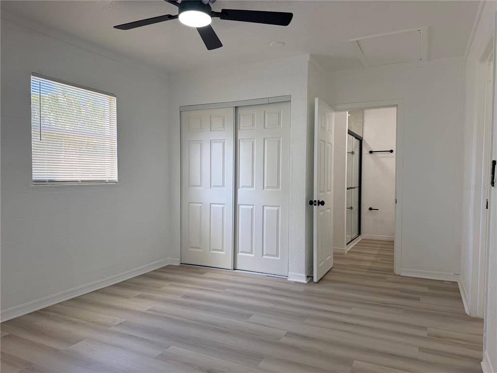 A bedroom with light wood-look flooring, a ceiling fan, a sliding closet, and an attached bathroom — 12022 CHUCK CIRCLE, HUDSON, FL