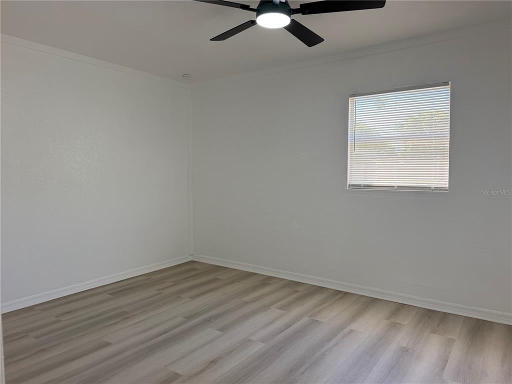 An empty bedroom features white walls, light wood-look flooring, a ceiling fan, and one window — 12022 CHUCK CIRCLE, HUDSON, FL