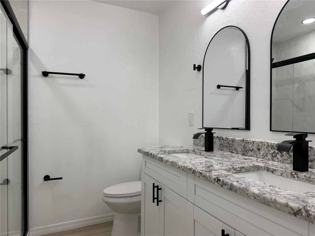 A bathroom features a double vanity with granite countertops, black fixtures, and arched mirrors — 12022 CHUCK CIRCLE, HUDSON, FL