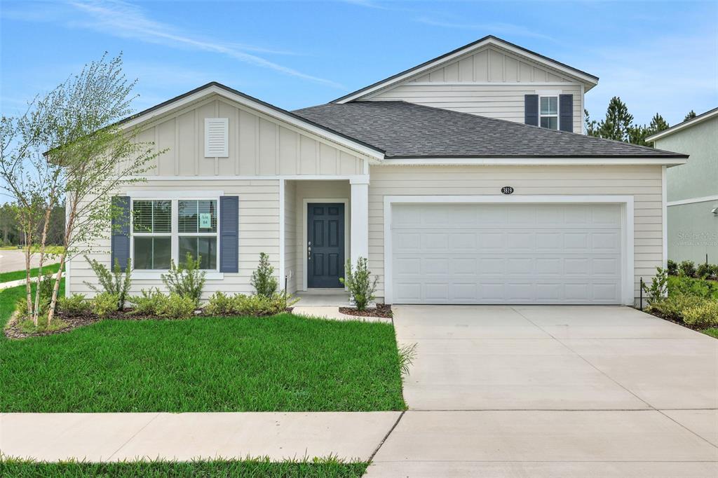 A single-story suburban house features light siding, a two-car garage, and a dark front door — 3819 HOLSTEIN WAY, GREEN COVE SPRINGS, FL