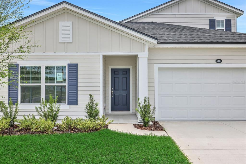 A single-story house exterior features light siding, a blue front door, and a two-car garage — 3819 HOLSTEIN WAY, GREEN COVE SPRINGS, FL