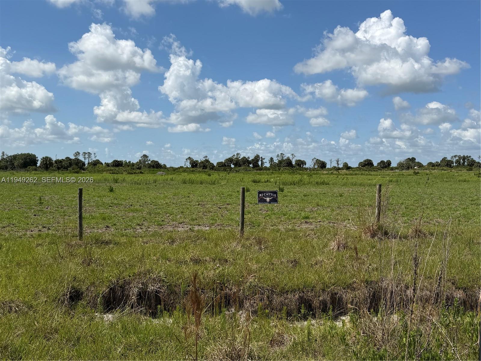 A fenced, grassy pasture under a blue sky with clouds features an RJ Cattle sign — 27325 NW 72, Okeechobee FL 34972, OKEECHOBEE, FL