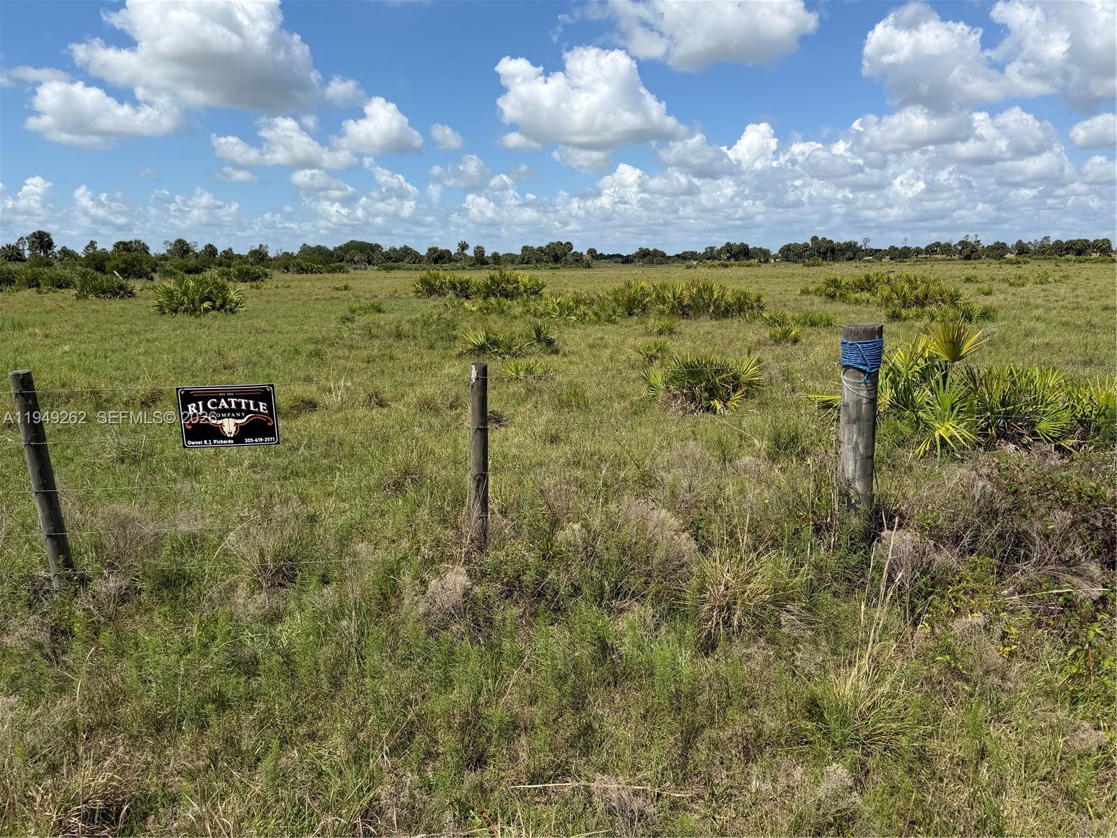 A barbed wire fence with a sign stands in a grassy field under a cloudy sky — 27325 NW 72, Okeechobee FL 34972, OKEECHOBEE, FL
