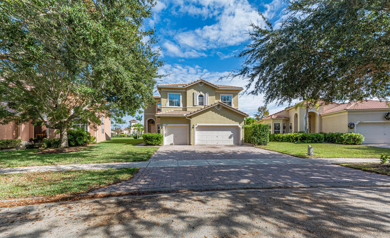 A two-story tan house with a three-car garage and a paved driveway under a blue sky — 6027 Arlington Way, Fort Pierce FL 34951, FORT PIERCE, FL