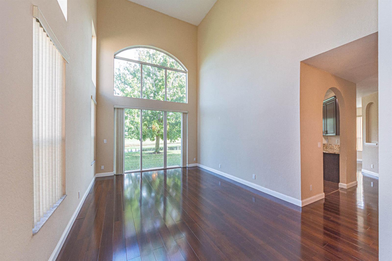An empty living room features high ceilings, dark hardwood floors, and a large arched window — 6027 Arlington Way, Fort Pierce FL 34951, FORT PIERCE, FL