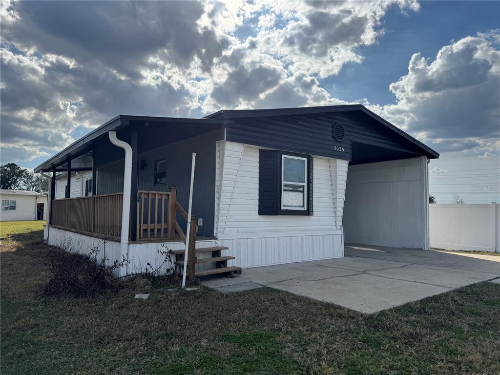 A single-story manufactured home features a covered porch, a carport, and white and dark siding — 5035 SOUTHSHORE DRIVE, POLK CITY, FL