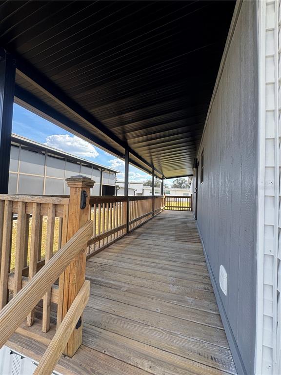 A long, covered wooden deck runs alongside the exterior wall of a gray house — 5035 SOUTHSHORE DRIVE, POLK CITY, FL
