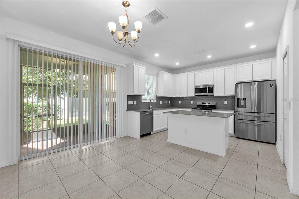 A kitchen with white cabinets, stainless steel appliances, a center island, and sliding glass doors — 5741 SPOTTED HARRIER WAY, LITHIA, FL