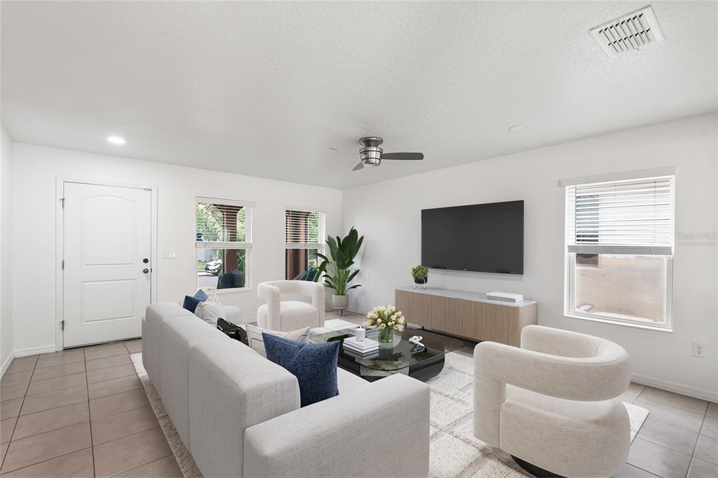 A bright living room features a light gray sofa, two white armchairs, and a television — 11309 BRIGHTON KNOLL LOOP, RIVERVIEW, FL