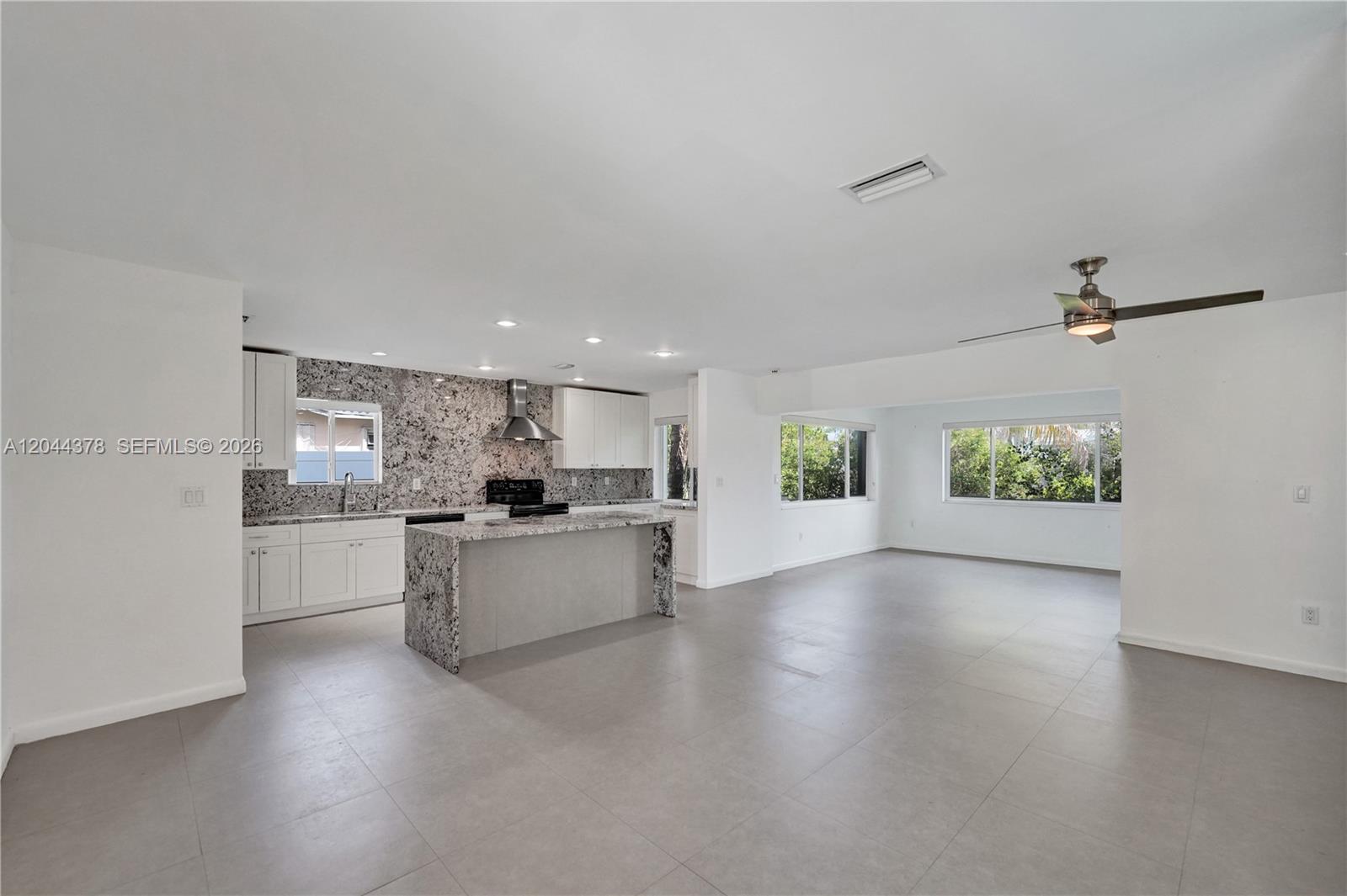 An open-concept kitchen and living area features white cabinets, granite countertops, and large floor tiles — 4311 Hayes St, Hollywood FL 33021, HOLLYWOOD, FL