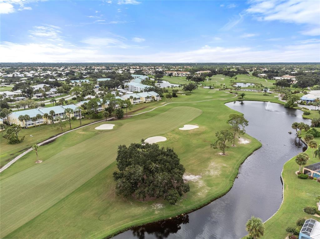 An aerial view shows a golf course fairway with sand traps, a pond, and surrounding buildings — 410 CERROMAR CIRCLE S UNIT 242, VENICE, FL