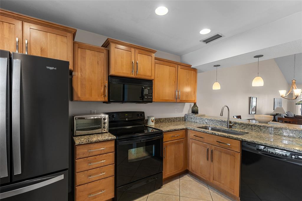 A kitchen with light wood cabinets, black appliances, and granite countertops — 410 CERROMAR CIRCLE S UNIT 242, VENICE, FL