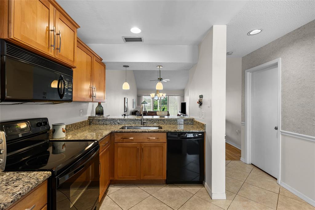 A kitchen features wood cabinets, granite countertops, black appliances, and tile flooring — 410 CERROMAR CIRCLE S UNIT 242, VENICE, FL