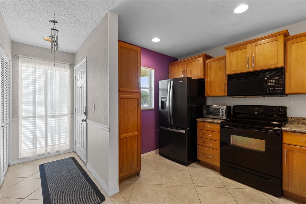 A kitchen with wood cabinets, black appliances, and a purple accent wall near a doorway — 410 CERROMAR CIRCLE S UNIT 242, VENICE, FL