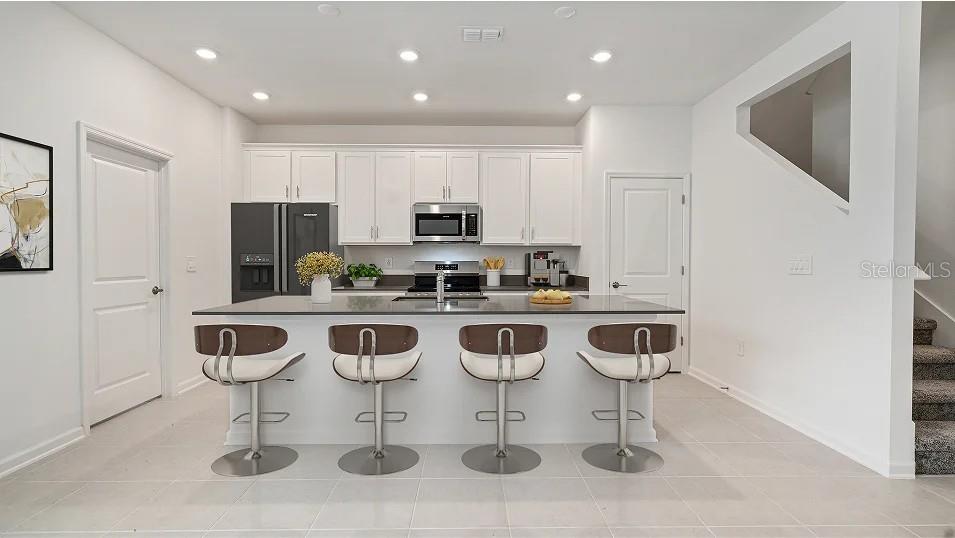 A modern kitchen features white cabinets, a gray island with four barstools, and tile flooring — 5553 RONIN DRIVE, ST CLOUD, FL