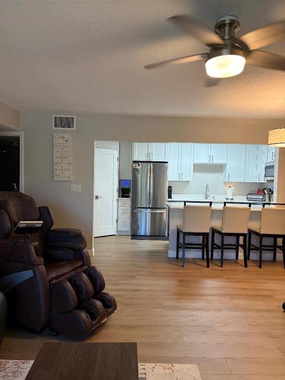 A living room with a brown massage chair leads into a kitchen with white cabinets — 1225 PINE RIDGE CIRCLE W UNIT C1, TARPON SPRINGS, FL