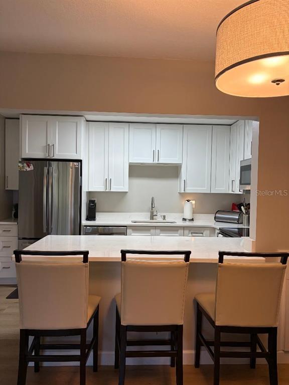 A kitchen features white cabinets, stainless steel appliances, and a breakfast bar with three chairs — 1225 PINE RIDGE CIRCLE W UNIT C1, TARPON SPRINGS, FL