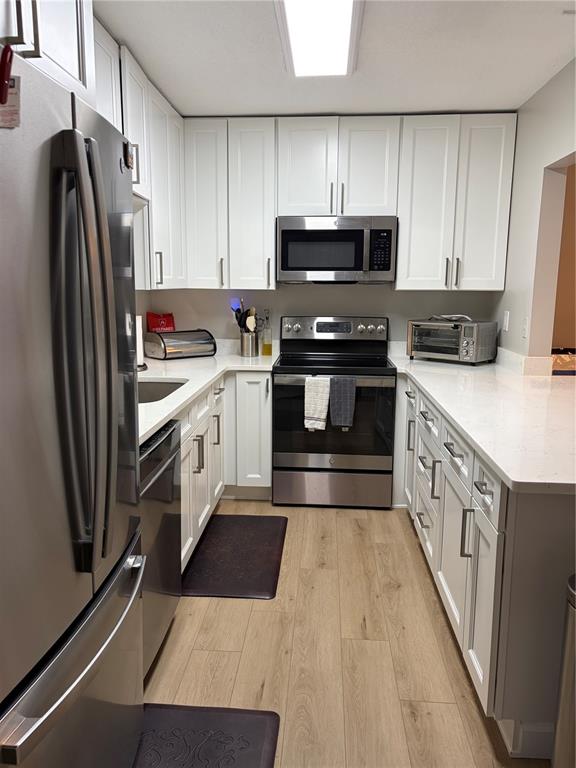 A galley kitchen features white cabinets, stainless steel appliances, and light wood-look flooring — 1225 PINE RIDGE CIRCLE W UNIT C1, TARPON SPRINGS, FL
