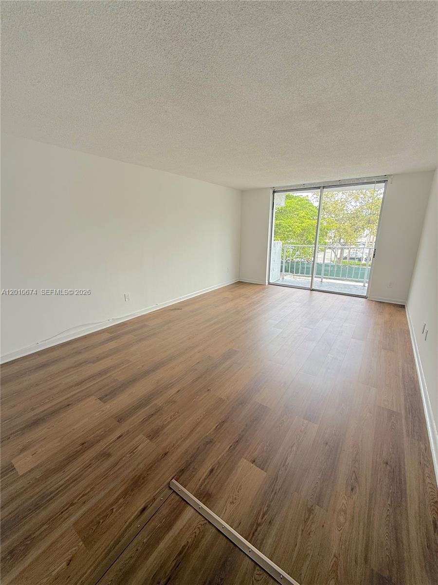 An empty room features light wood-look flooring, white walls, and a sliding glass balcony door — 482 NW 165th St Rd # 307, Miami FL 33169, MIAMI, FL