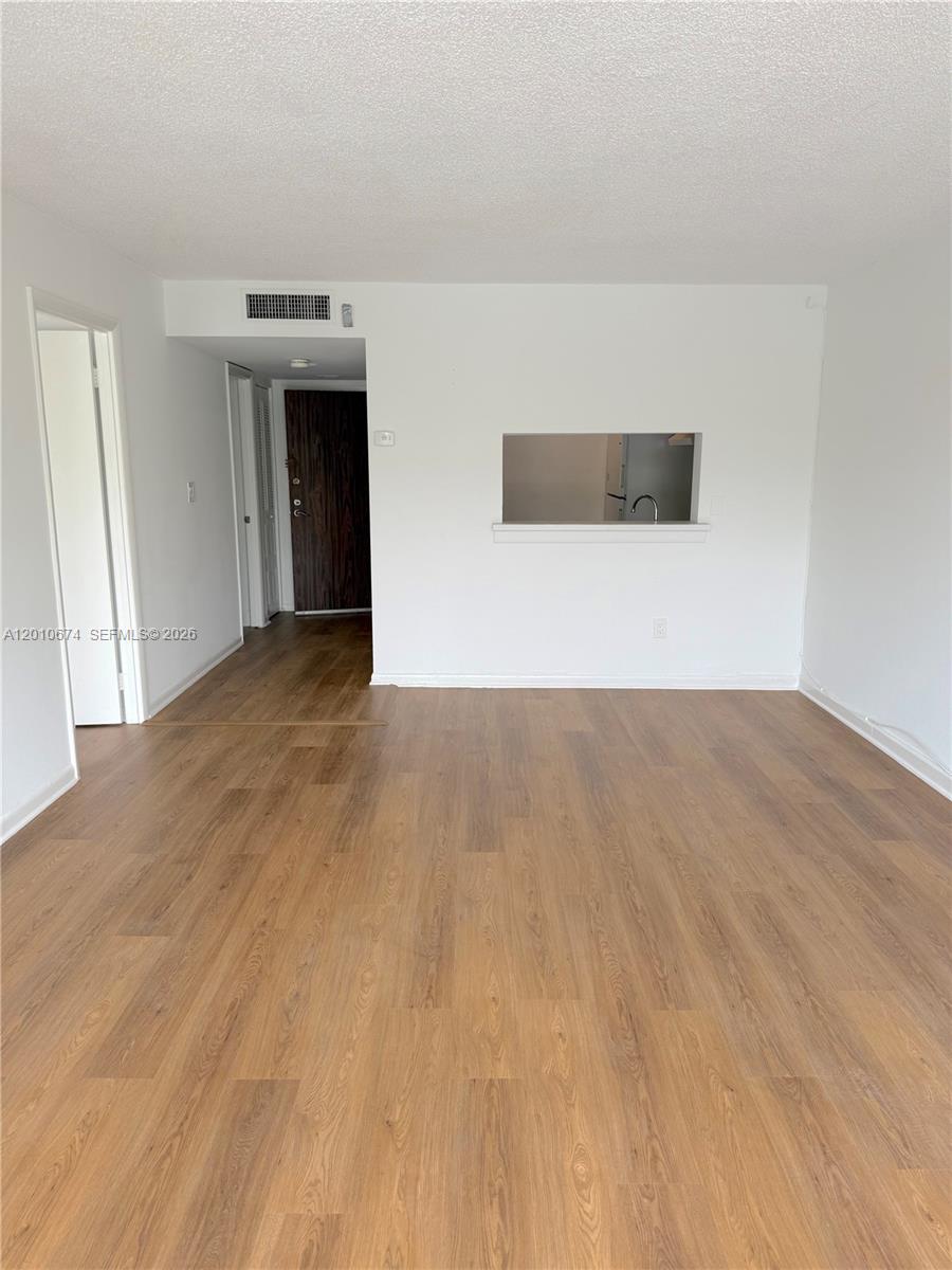 An empty room with wood-look flooring, white walls, and a pass-through window to the kitchen — 482 NW 165th St Rd # 307, Miami FL 33169, MIAMI, FL